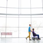 Young man pushing his girlfriend in wheelchair outdoors after shopping at mall