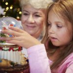 Senior with girl watching christmas snow globe