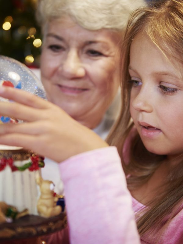 Senior with girl watching christmas snow globe